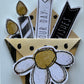 A handmade scrapbook paper embellishment featuring a white daisy with a gold center, black and white banners reading 'WISHES' and 'OUR DAY', and gold foil leaf accents on a white paneled background.